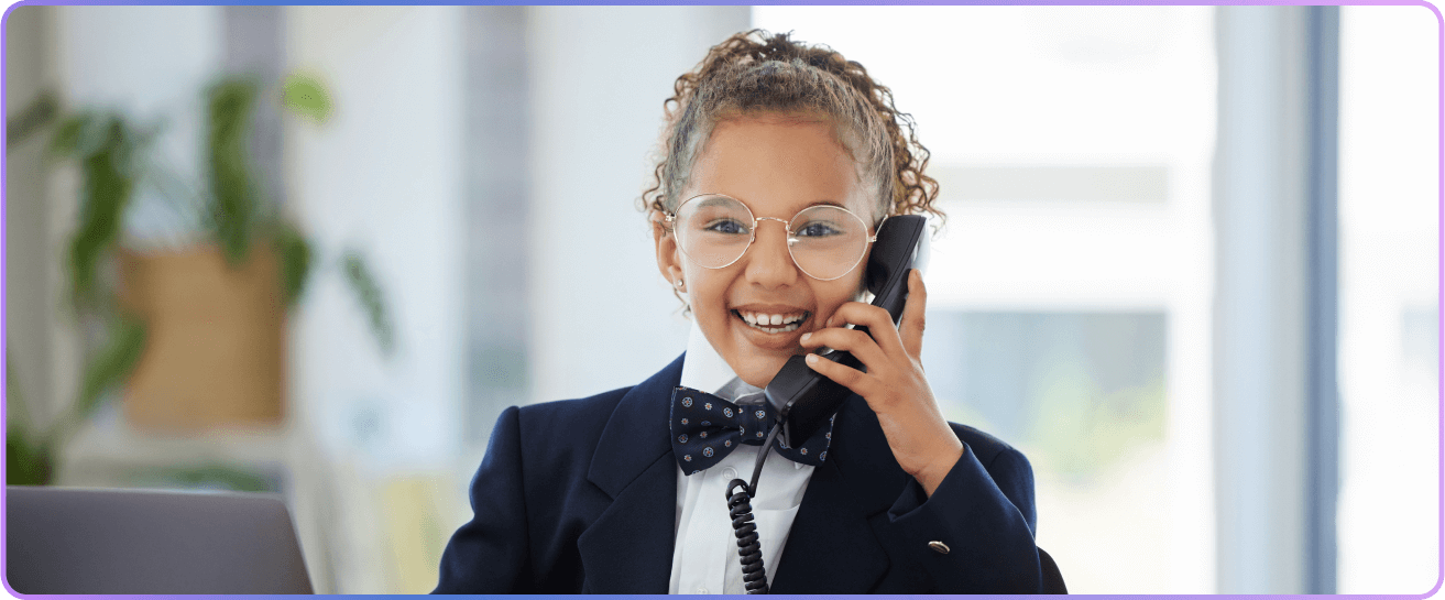 A young girl in a suit and bow tie smiling while talking on the phone